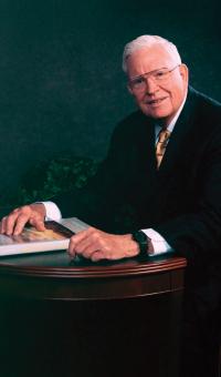George H. Gordon seated in suit at table with hand on book 