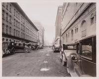 View looking down street with tall buildings and cars parked on sides